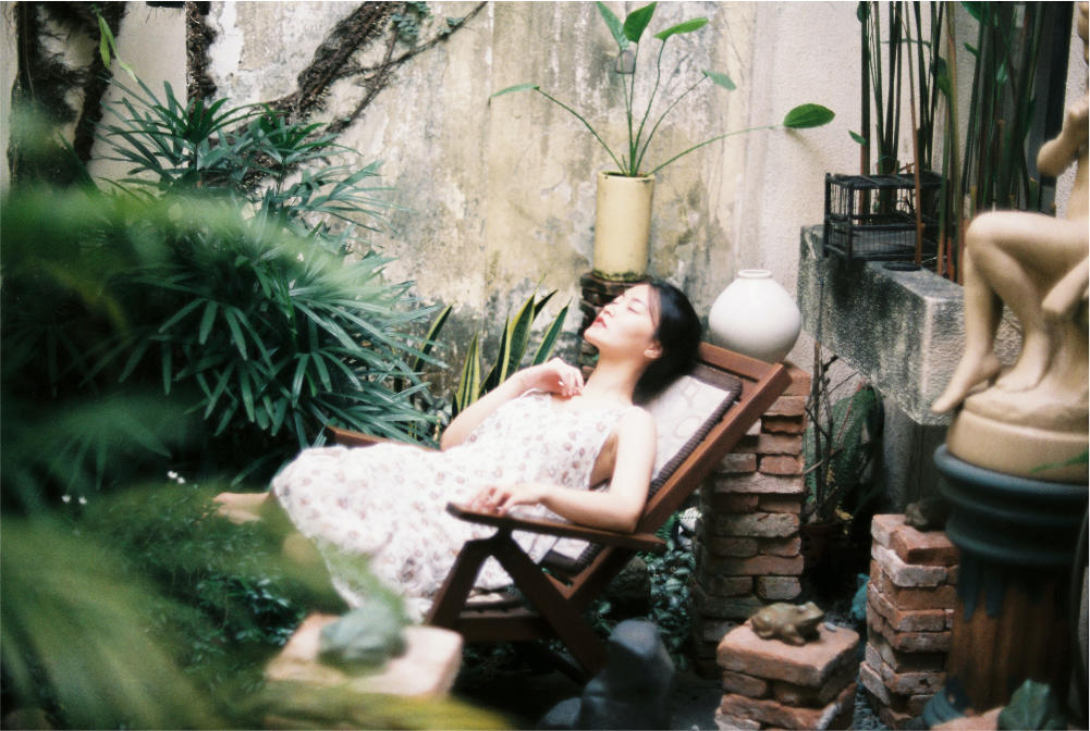 asian woman relaxing in a folded chair, in a rustic themed back garden with eyes closed